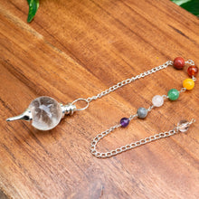 Load image into Gallery viewer, "Clear Quartz Crystal Pendulum with a crystal chip chain on a wooden plank," - Down to Earth.
