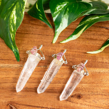 Load image into Gallery viewer, "Three crystal pendants on a wooden surface with green leaves in the background," - Down to Earth.
