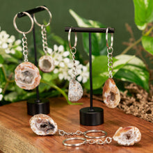 Load image into Gallery viewer, Assorted Crystal Geode Keychain displayed on a wooden surface with a colorful background low angle - Down to Earth
