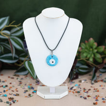 Load image into Gallery viewer, Evil eye ligth blue varient necklaces on a white mannequin neck against a green background - Down to Earth
