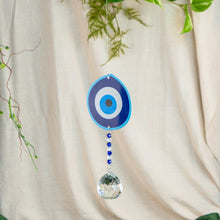 Load image into Gallery viewer, "Decorative hanging with blue and white eye design and crystal ball on a beige curtain background," - Down to Earth.
