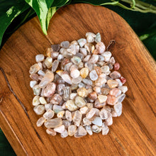 Load image into Gallery viewer, "Flower Agate Crystal Chips on a wooden base with green foliage in the background," - Down to Earth.
