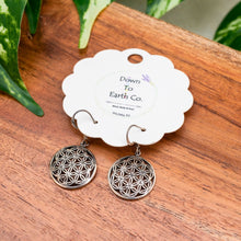 Load image into Gallery viewer, "Sterling Silver Flower of Life earrings on a 'Down To Earth Co.' branded card on a wooden surface with green leaves," - Down to Earth.
