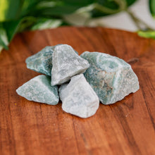 Load image into Gallery viewer, Green Aventurine Rough crystals on a wooden surface with blurred greenery in the background - Down to Earth 
