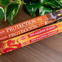 Load image into Gallery viewer, "Two boxes of HEM incense sticks labeled 'Protection' and 'Dragons Blood' on a wooden surface with green leaves in the background," - Down to Earth.
