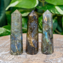Load image into Gallery viewer, "Three Labradorite Towers on a wooden base with green foliage in the background. This crystal is widely used in the metaphysical community for its transformative properties," - Down to Earth.
