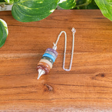 Load image into Gallery viewer, Layered 7 Charka Pendulum top down angled with plants on a style background - Down To Earth
