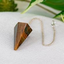Load image into Gallery viewer, Tiger’s Eye Faceted Pendulum on a light shaded cloth with greenery in the background lower angle - Down to Earth
