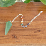 Premiere Green Aventurine Faceted Pendulum with 7 Chakra angled with plants on a styled background - Down To Earth