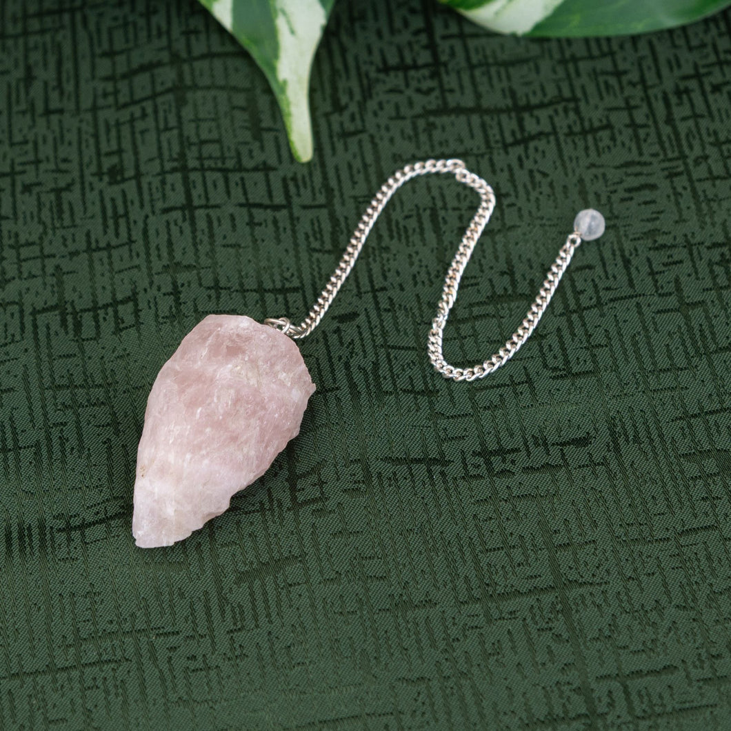 Raw Rose Quartz Pendulum on a green background - Down to Earth 