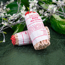 Load image into Gallery viewer, Rose Rope Incense stacked against each other on a green cloth with flowers in the background - Down to Earth
