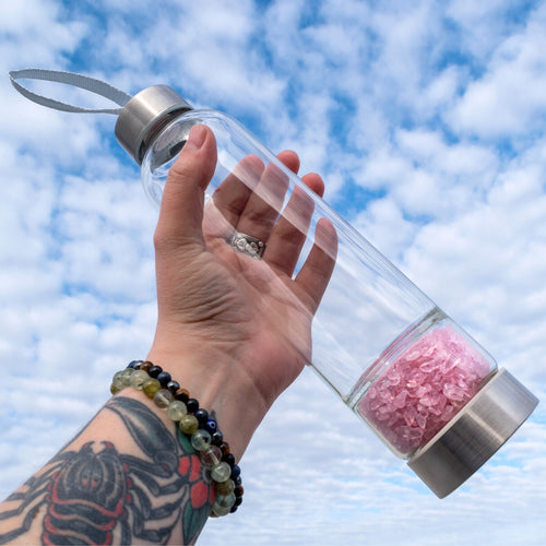 Rose Quartz Water Bottle in Hand with Blue Sky and Clouds in the background - Down To Earth