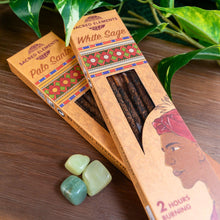 Load image into Gallery viewer, "Two boxes of Sacred Elements Incense Sticks laid on top of a wooden surface next to three green gemstones with foliage in the background," - Down to Earth.
