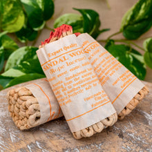 Load image into Gallery viewer, &quot;Three bundles of sandalwood incense wrapped in brown paper with orange text, placed on a wooden surface with green leaves in the background,&quot; - Down to Earth.
