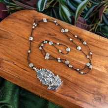 Load image into Gallery viewer, "Silver Ganesh Necklace on a wooden surface with green foliage in the background," - Down to Earth.
