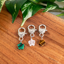 Load image into Gallery viewer, "Three silver charms with gemstones on a wooden surface with leaves in the background," - Down to Earth.

