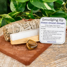 Load image into Gallery viewer, "Tiger's Eye Smudging Kit that includes a tumbled Tiger's Eye, Palo Santo, White Sage, a 4'' Selenite Wand, an info card, and a brown organza bag," - Down to Earth.
