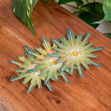Load image into Gallery viewer, "Three Triple Moon Crystal Holographic Stickers on a wooden plank with green foliage in the background," - Down to Earth.
