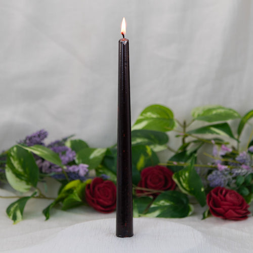 Vampire Blood Candle, a flame on a white surface with greenery and flowers in the background - Down to Earth