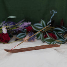 Load image into Gallery viewer, Vampire Blood Incense Stick lit on a holder with a floral background - Down to Earth 
