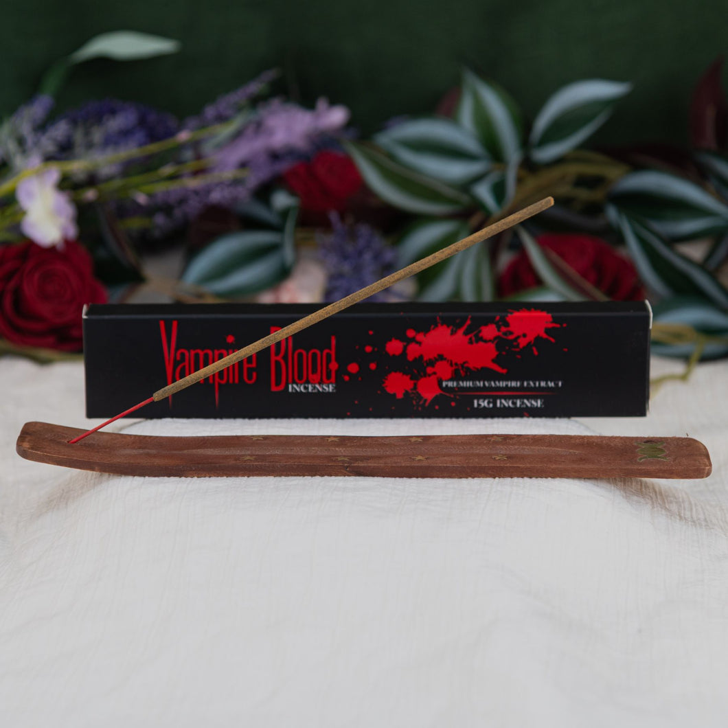 Vampire Blood Incense Stick lit on a holder with box in background with a floral background - Down to Earth 