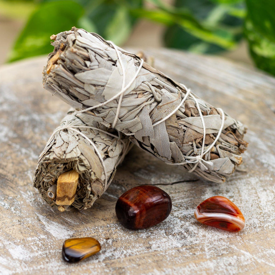 "Two bundles of white sage with palo santo sticks lay on top of each other. There are three crystals in front of the smudge sticks." - Down to Earth.