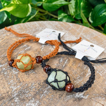 Load image into Gallery viewer, "Two Adjustable Crystal Bracelets in brown and black on a wooden plank with green foliage in the background," - Down to Earth.
