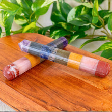 Load image into Gallery viewer, "Colorful crystal wand on a wooden surface with green plants in the background," - Down to Earth.
