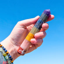 Load image into Gallery viewer, "Hand holding a multicolored crystal wand against a clear blue sky," - Down to Earth.
