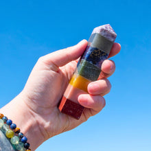 Load image into Gallery viewer, "Hand holding a chakra stone tower against a clear blue sky," - Down to Earth.
