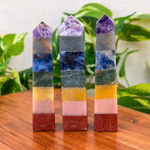 Load image into Gallery viewer, "Three Chakra Towers on a wooden platform with green foliage in the background," - Down to Earth.
