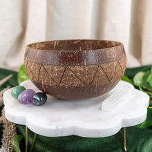 Load image into Gallery viewer, "Coconut bowl on a white marble stand with stones and greenery," - Down to Earth.
