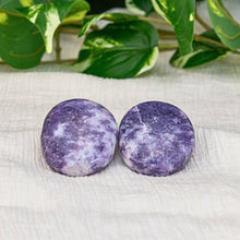 Load image into Gallery viewer, &quot;Two large lepidolite crystal palm stones on a cream-colored sheet with foliage in the background,&quot; - Down to Earth.

