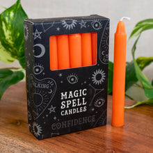 Load image into Gallery viewer, "Box of 'Magic Spell Candles' labeled 'Confidence' with an orange candle on a wooden surface," - Down to Earth.
