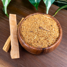 Load image into Gallery viewer, "Wooden bowl filled to the brim with ground Palo Santo Powder with two Palo Santo sticks next to the bowl with green foliage in the background," - Down to Earth.
