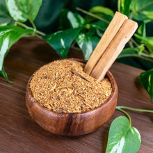 Load image into Gallery viewer, "Wooden bowl filled to the top with crushed Palo Santo powder with two sticks of Palo Santo stuck inside the powder with green foliage in the background," - Down to Earth.
