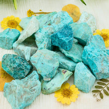 Load image into Gallery viewer, &quot;Close-up of a pile of raw turquoise crystals surrounded by yellow flowers,&quot; - Down to Earth.
