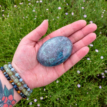 Load image into Gallery viewer, &quot;An open palm holding a large Ruby in Kyanite palm stone with greenery in the background,&quot; - Down to Earth.
