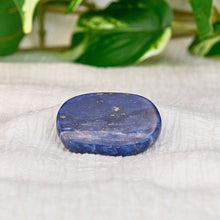 Load image into Gallery viewer, &quot;A flat sodalite palm stone on top of a cream-colored cloth with foliage in the background,&quot; - Down to Earth.
