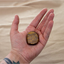Load image into Gallery viewer, Picture of a tiger&#39;s eye palm stone being held in a hand. - Down to Earth.
