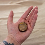 Picture of a tiger's eye palm stone being held in a hand. - Down to Earth.