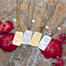 Load image into Gallery viewer, "Four Zodiac Necklaces in both gold and silver surrounded by red flowers on a wooden plank," - Down to Earth.
